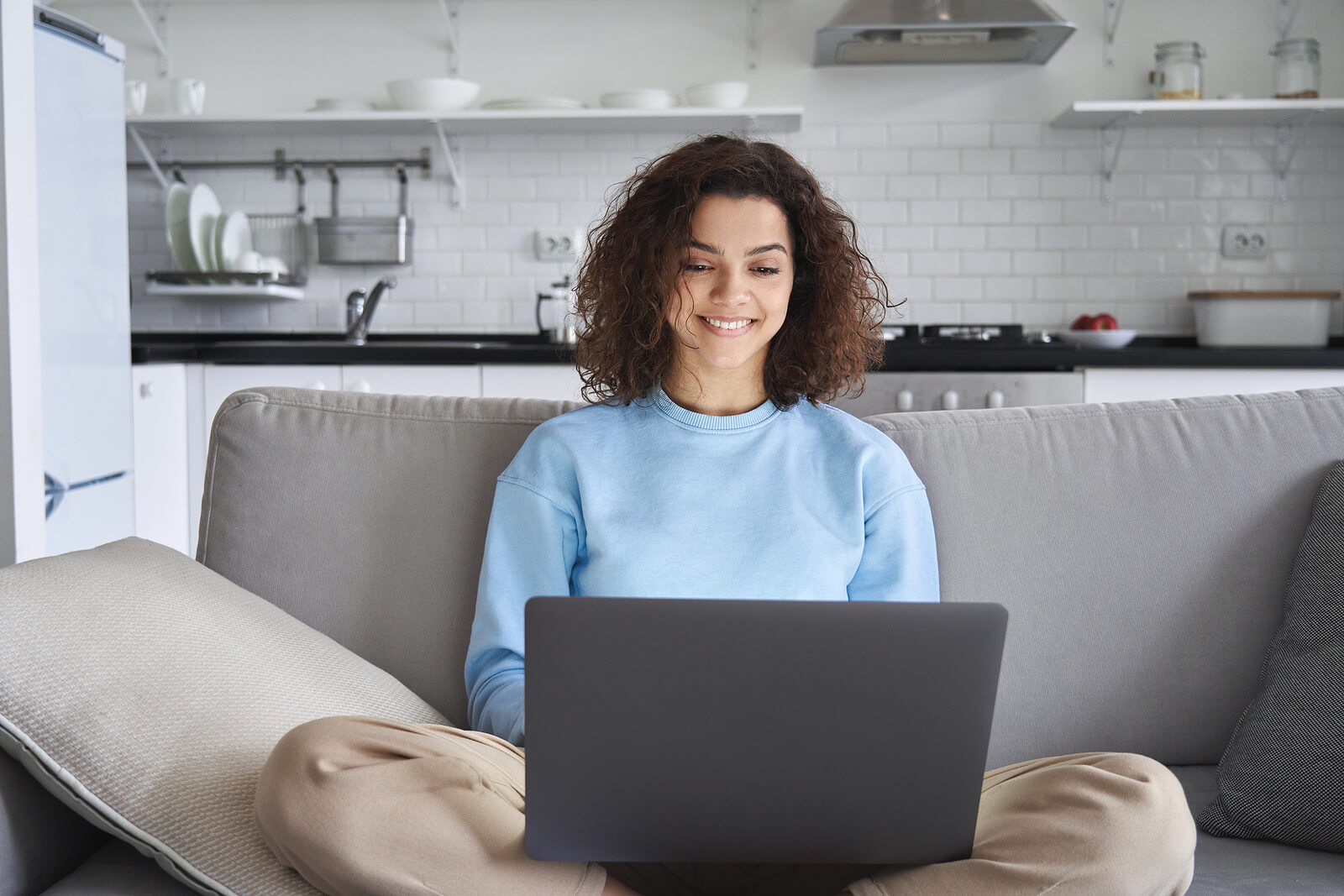 A woman sits on a couch while typing on a laptop and smiling. Looking to begin anxiety treatment in Evanston, IL? Speak with our anxiety therapist to begin working through your social anxiety. 