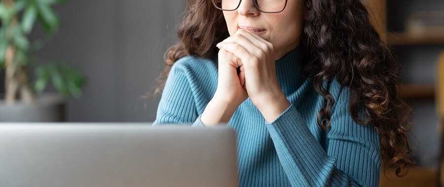 A woman sits facing her laptop but looking outside. Trying to figure out if counseling for college students is right for you? Speak with our therapist for college students in Illinois to learn more!
