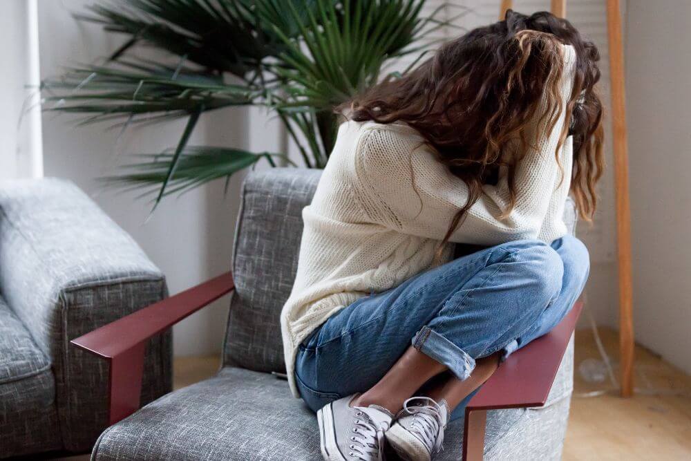 Teenager curled up in a chair with her head in her hands. The photo symbolizes the pain of teen anxiety. Get therapy for teen anxiety in Evanston IL | 60201