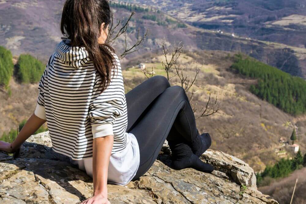 A woman sits on the edge of a cliff overlooking trees. Looking for a way to get past your anxiety? Therapy for anxiety in Evanston, IL might be the right choice for you. Conquer your anxiety with an anxiety therapist today!