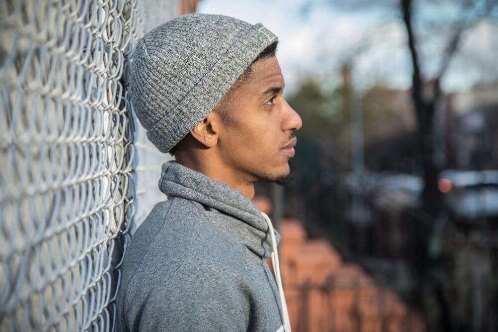 Young thoughtful man leaning against a fence. The photo represents a young adult thinking about his future. Therapy for Young adults in Evanston IL can help you make the big decisions. Find direction at Evanston Counseling | 60201