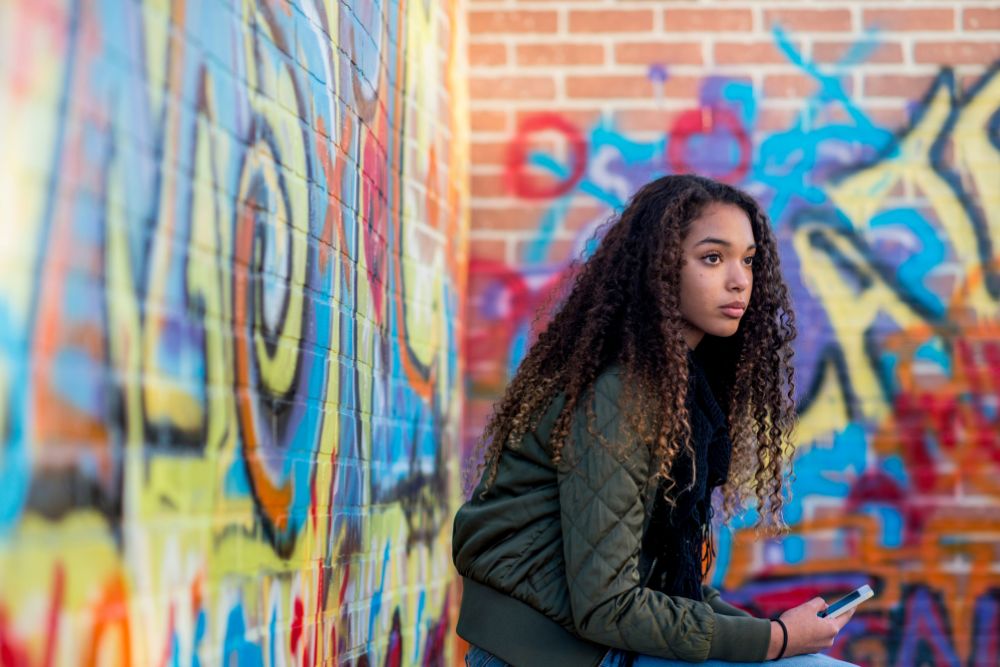 A teenage girl sits near a colorful wall while thinking. Noticing the signs that your teen might need Online Therapy for Teenagers in Evanston, IL? Talk with a therapist for teens in Illinois to learn how you can help your teen!