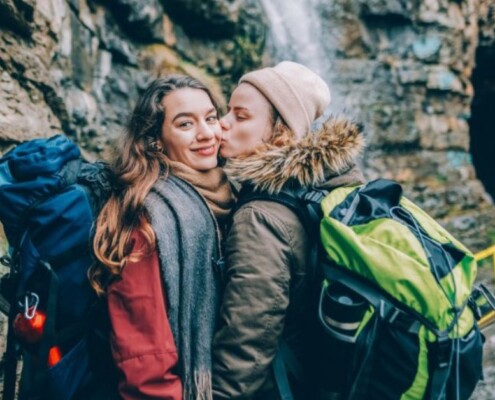 A woman kisses another woman's cheek while hiking. Wondering if LGBTQ+ Affirming therapy in Evanston, IL is right for you? Speak with an LGBTQIA+ affirming therapist in Illinois to see how therapy can help you!