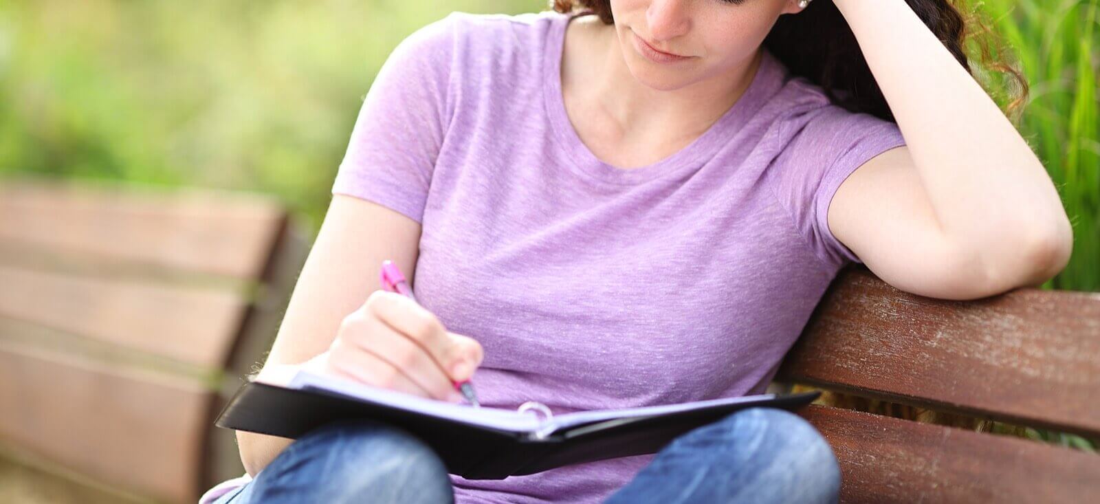 A young woman sits on a park bench while writing in a journal. Want to see how Therapy for College Students helps navigate Life Transitions in Evanston, IL? Speak to a therapist for college students today to learn more!