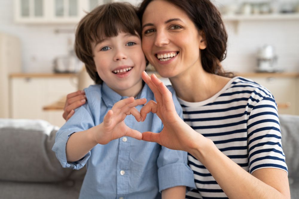 A mom and her young son sit on a couch making a heart with their hands. Struggling with life changes as a mom? Speak with a therapist for moms to see how Therapy for Moms in Evanston, IL can help you!