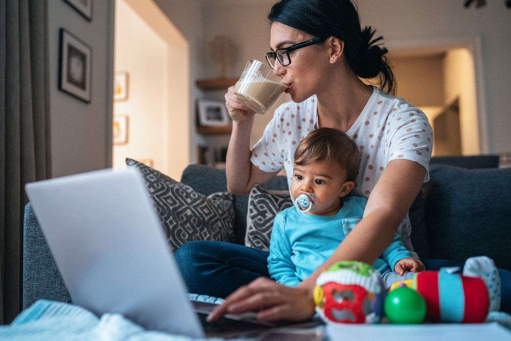 Mom working on laptop, sipping coffee, while holding baby. Want to manage your mom anxiety better? It might be time to seek out therapy for moms in Evanston, IL. Speak with a therapist for moms today!