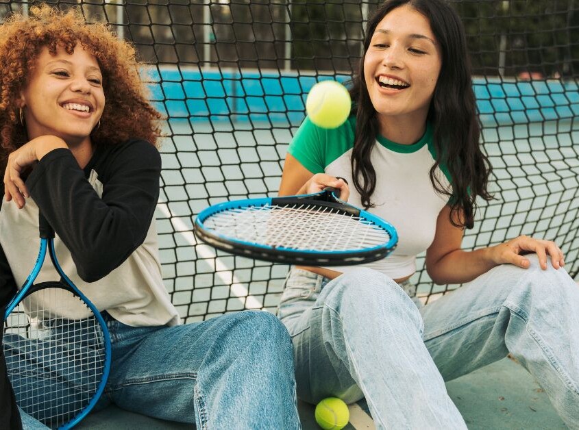 Two teen girls sit on the ground playing with a tennis ball together. Want to help your teen better understand themselves? Speak with a teen therapist to see how teen therapy in evanston, IL can help them.