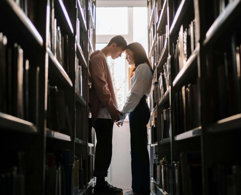 A college couple stands close together in a library, reflecting on the highs and lows of dating. Learn how therapy for college students in Chicago, IL and therapy for young adults in Chicago, IL can support emotional well-being in relationships.