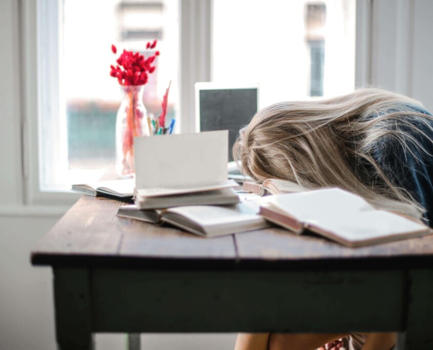 A stressed teen with their head on a desk surrounded by books, overwhelmed with emotions. Learn how an Evanston teenage therapist and teen therapy in Evanston, IL can provide support.