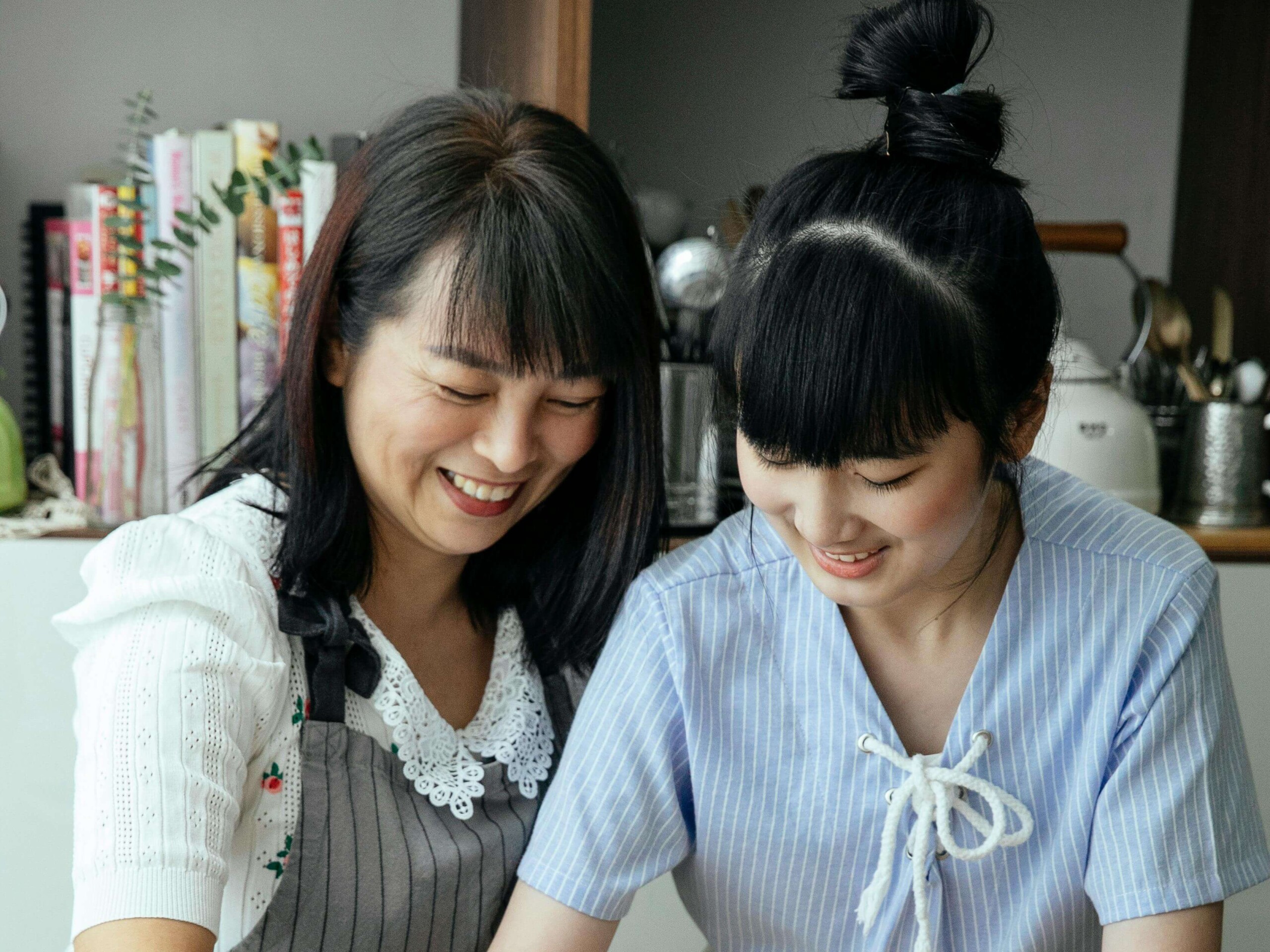Mother and teenage daughter smiling together in the kitchen, representing the positive connection that can grow through teen counseling in Evanston, IL and the support available through online therapy for moms in Chicago, IL.