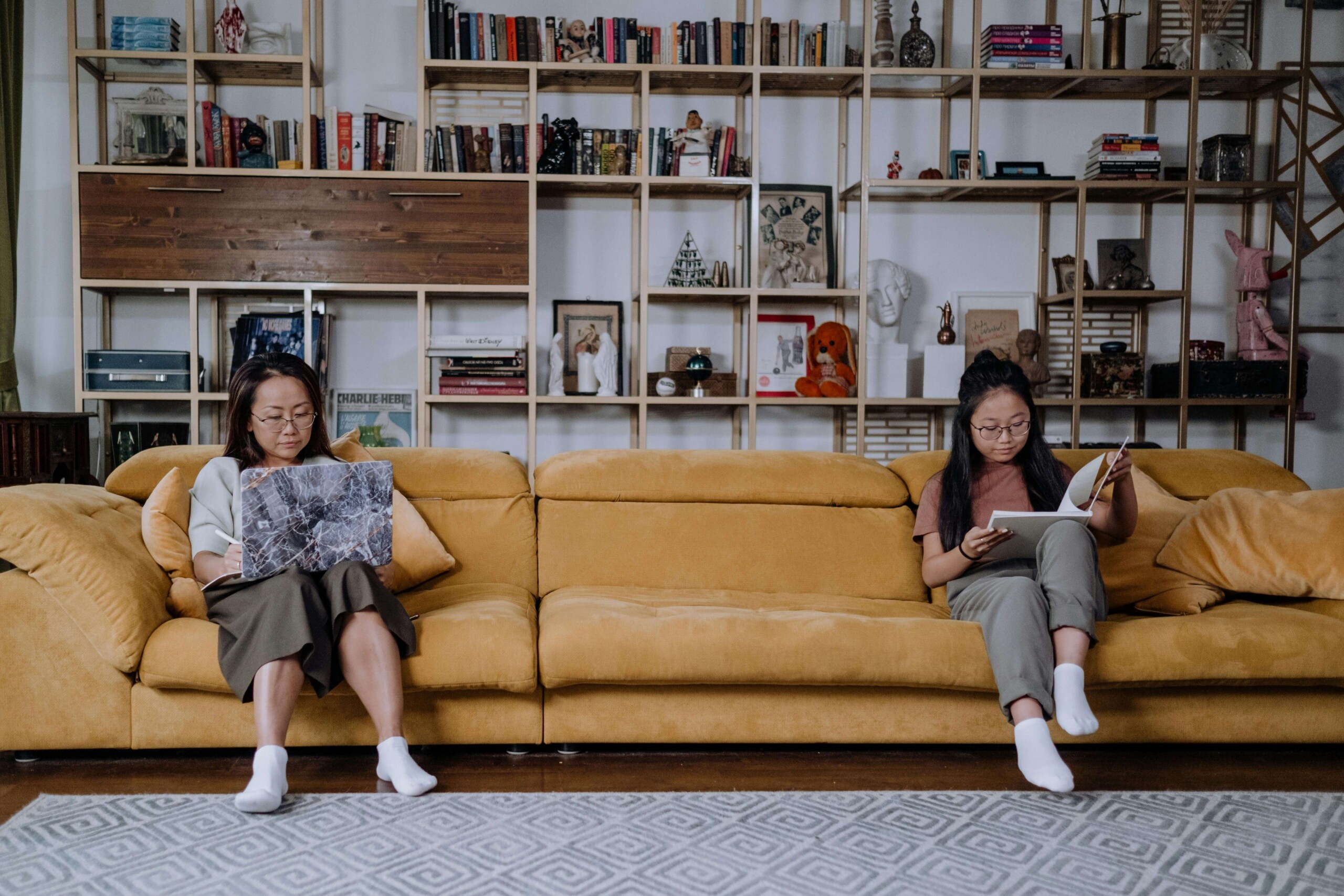 A mother and teen daughter sit at opposite ends of a couch, each absorbed in reading, reflecting the quiet distance that can come with anxiety. This image represents how maternal mental health in Evanston, IL and online therapy for moms in Chicago, IL can offer support in emotionally complex moments.