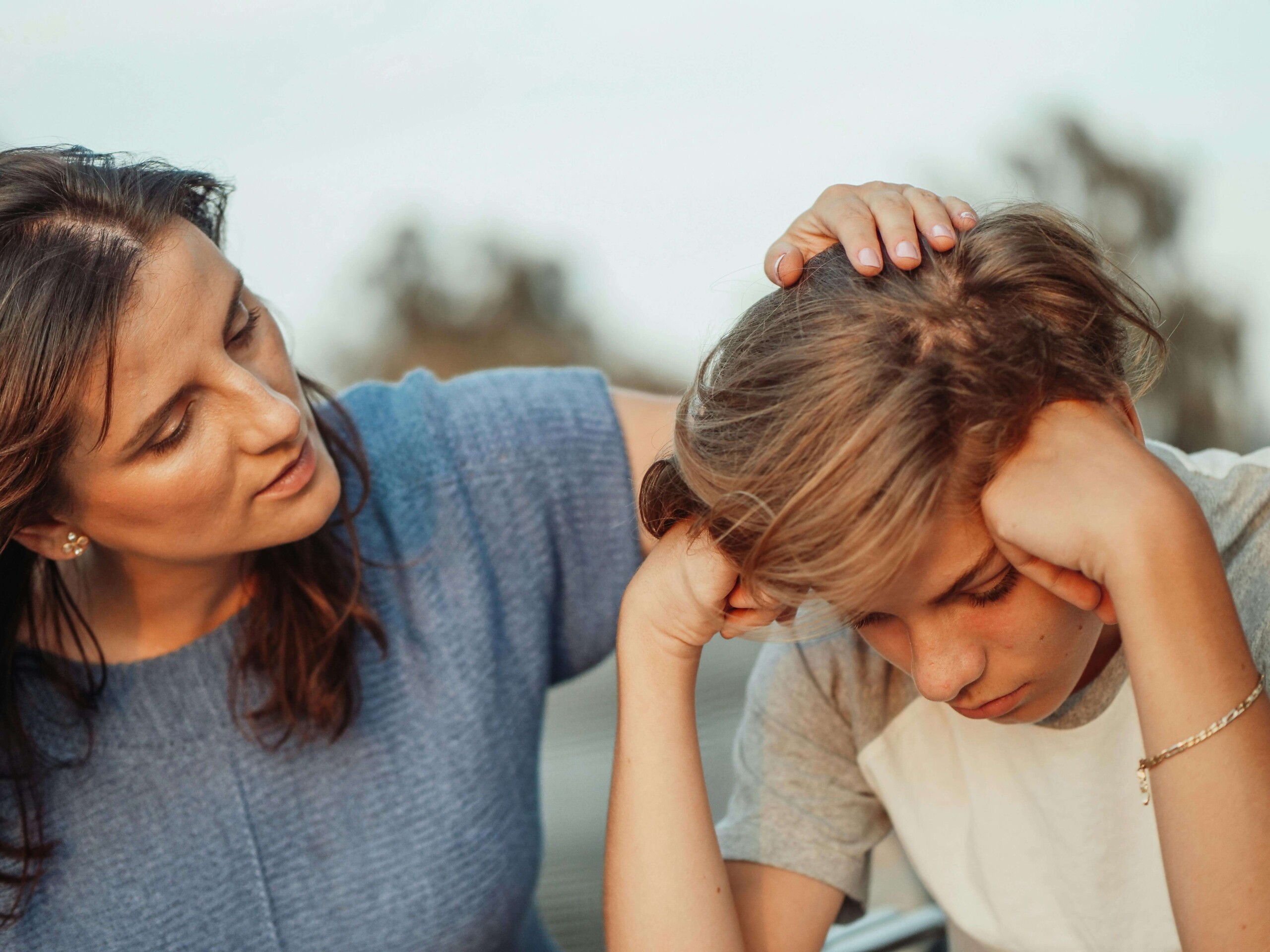 Mother gently comforts her overwhelmed teen, both seated outside during a moment of connection—capturing the emotional weight that therapy for teens in Chicago, IL and support for maternal mental health in Evanston, IL can help address.