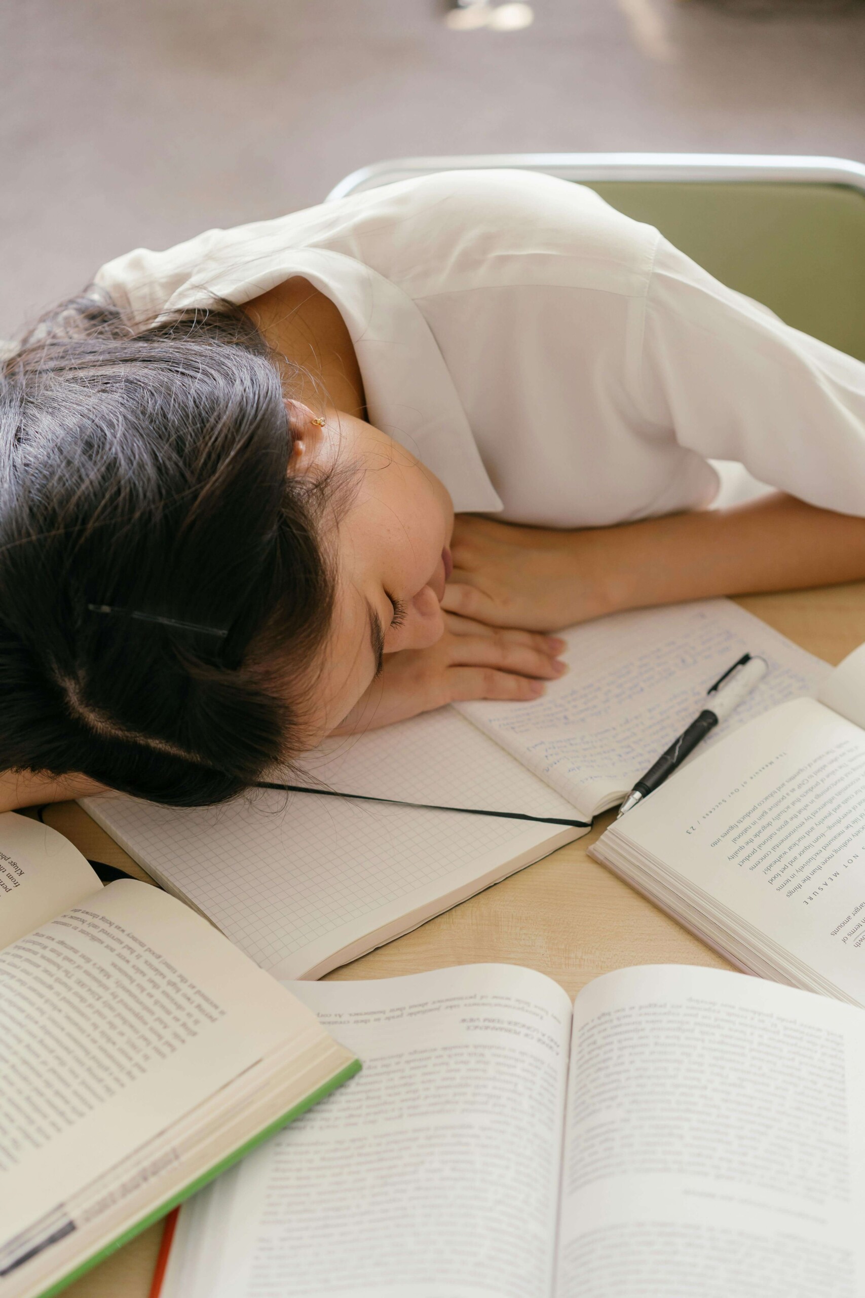 Teen girl asleep on open textbooks at a desk, overwhelmed by academic pressure—representing the need for therapy for teens in Chicago, IL and therapy for young adults in Chicago, IL.