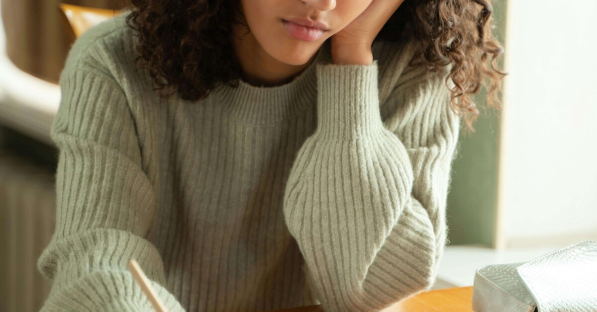 Teen girl looking stressed while studying at a desk, representing the emotional challenges many adolescents face—support is available through a therapist for teens in Evanston, IL, especially when school anxiety overlaps with maternal mental health in Evanston, IL.