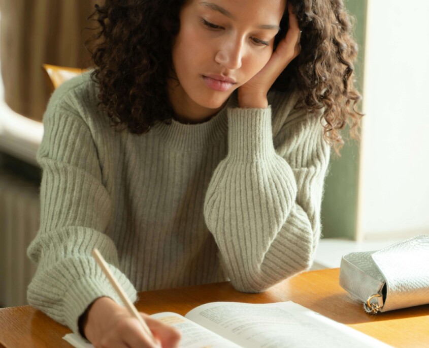 Teen girl looking stressed while studying at a desk, representing the emotional challenges many adolescents face—support is available through a therapist for teens in Evanston, IL, especially when school anxiety overlaps with maternal mental health in Evanston, IL.