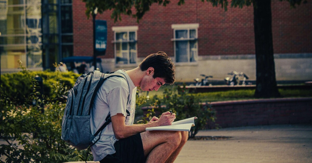 College student sitting alone on campus steps with a notebook and backpack, reflecting the academic and emotional pressures discussed in therapy for college students in Chicago, IL, with support from a therapist for college students in Chicago, IL.