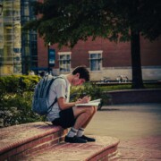 College student sitting alone on campus steps with a notebook and backpack, reflecting the academic and emotional pressures discussed in therapy for college students in Chicago, IL, with support from a therapist for college students in Chicago, IL.