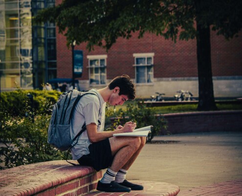 College student sitting alone on campus steps with a notebook and backpack, reflecting the academic and emotional pressures discussed in therapy for college students in Chicago, IL, with support from a therapist for college students in Chicago, IL.