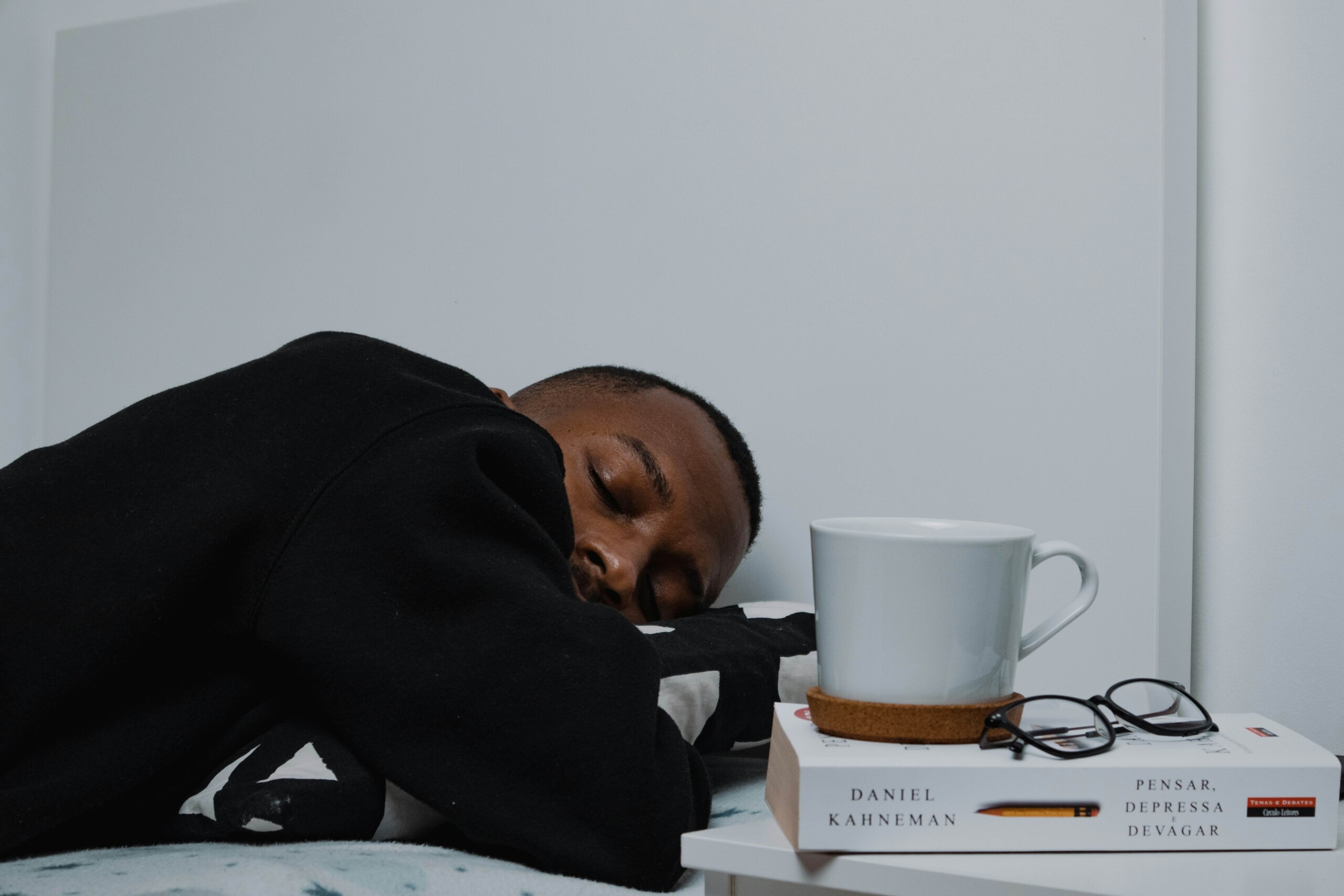 A college student resting on a bed next to a book and coffee mug, showing signs of burnout and exhaustion—highlighting the need for therapy for college students in Chicago, IL and support from a therapist for college students in Chicago, IL.