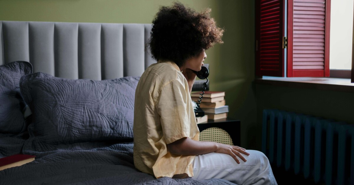 College student sitting on their bed while talking on the phone, appearing overwhelmed and in need of support — representing therapy for college students in Chicago, IL and the value of working with a therapist for college students in Chicago, IL.