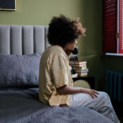 College student sitting on their bed while talking on the phone, appearing overwhelmed and in need of support — representing therapy for college students in Chicago, IL and the value of working with a therapist for college students in Chicago, IL.