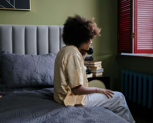 College student sitting on their bed while talking on the phone, appearing overwhelmed and in need of support — representing therapy for college students in Chicago, IL and the value of working with a therapist for college students in Chicago, IL.