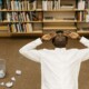 Overhead view of a college student lying on the floor in a library, surrounded by books and crumpled papers, symbolizing academic stress. Perfect visual for a blog on how cognitive behavioral therapy in Chicago, IL, and therapists for college students in Chicago, IL, can help manage academic pressure.
