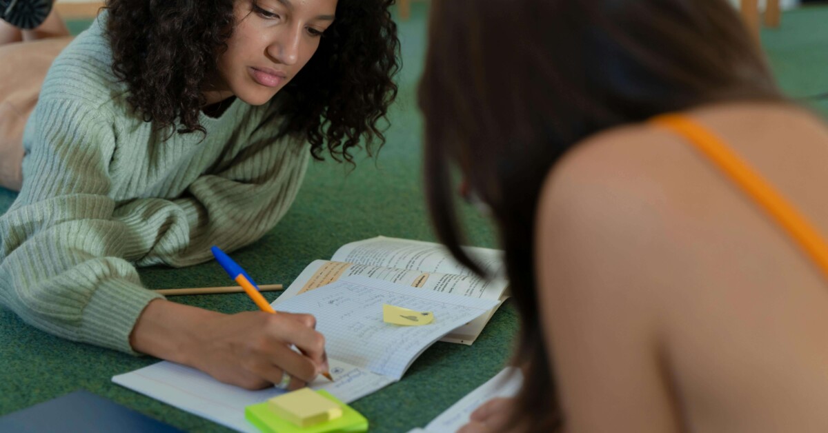 Two college students study together on the floor of a library, highlighting the pressures of academic life and the need for therapy for college students in Chicago, IL, with support from a therapist for college students in Chicago, IL.