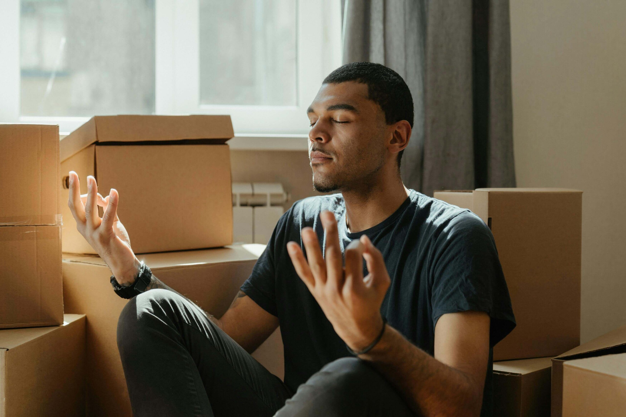 Meditating in Old Room | mental health resources in evanston, il | therapy for college students in chicago, il | therapist for college students in chicago, il | cognitive behavioral therapy in chicago, il | Central Street District, IL | Winnetka, IL | Gold Coast, IL A young Black man meditates on the floor surrounded by moving boxes, bathed in sunlight. Cognitive behavioral therapy in Chicago, IL, and mental health resources in Evanston, IL, can provide tools for managing family holiday stress and transitions.