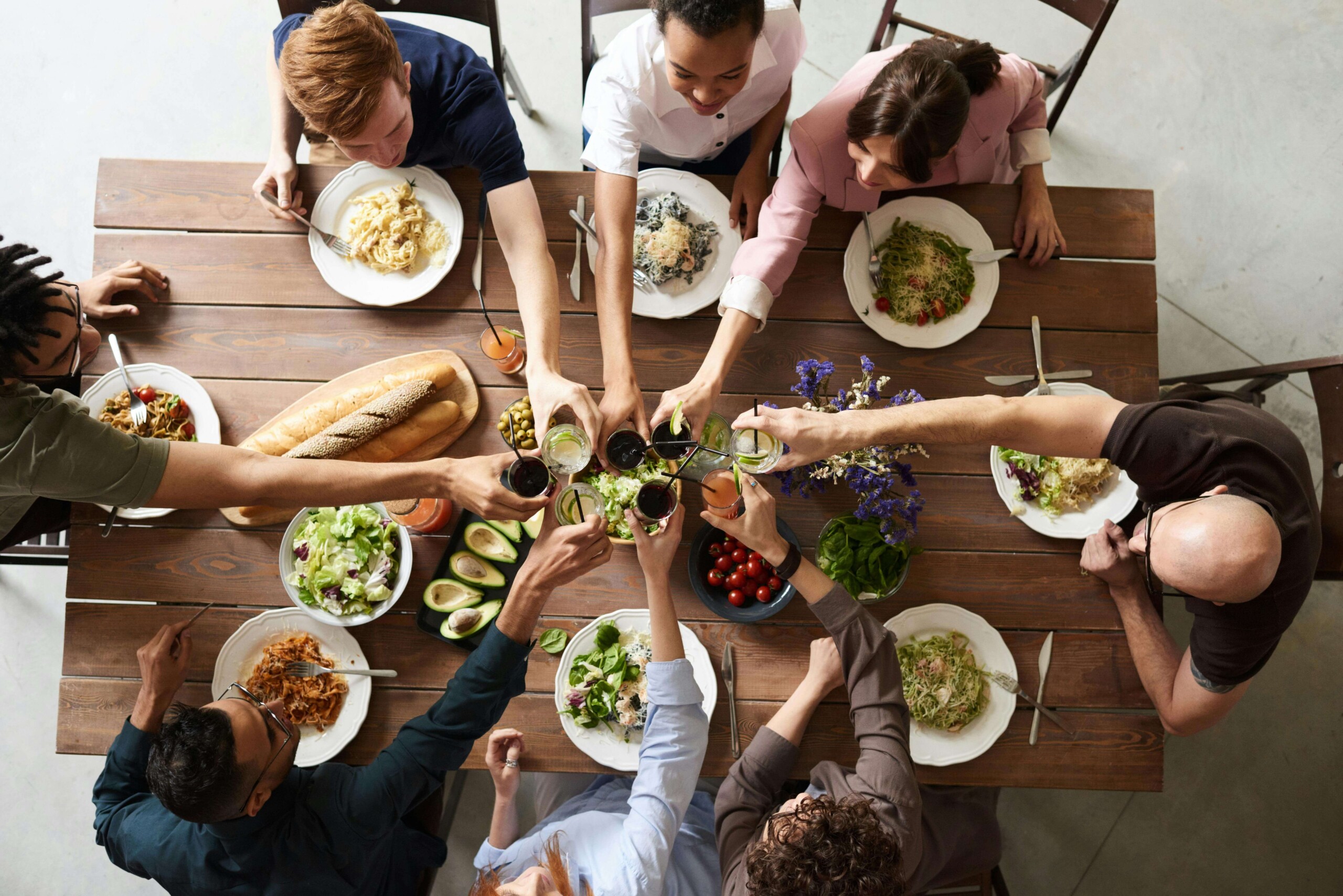 A diverse group of people gathers around a table, sharing a meal and raising glasses in a toast. Life transitions in Evanston, IL, and online therapy for college students in Chicago, IL, can provide support during family holiday challenges.