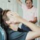 A young man sits in a chair, covering his face, while an older man stands in a doorway, gesturing with concern. Cognitive behavioral therapy in Chicago, IL, and a young adult therapist in Illinois can help families navigate holiday conflicts and improve communication.