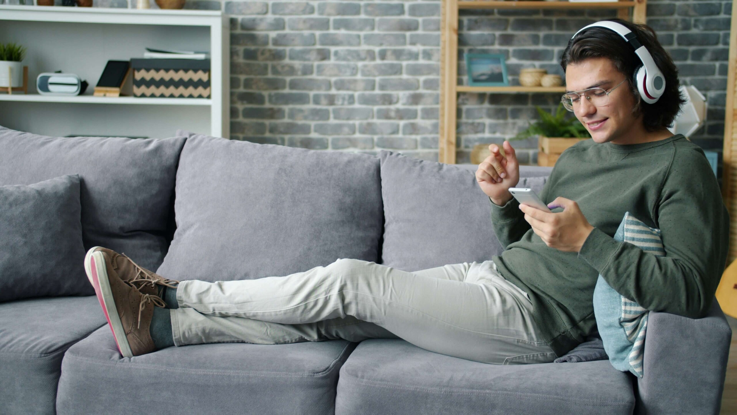 Relaxing on the Couch | cognitive behavioral therapy in chicago, il | therapist for college students in chicago, il | treatment for chronic pain in evanston, il | life transitions in evanston, il | Central Street District, IL | Winnetka, IL | Gold Coast, IL Young man relaxing on a gray sofa with headphones and a smartphone, symbolizing the benefits of online therapy for college students in Chicago, IL, and cognitive behavioral therapy in Chicago, IL, for setting holiday boundaries and managing family conflict.