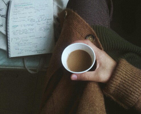 Overhead view of a student holding coffee beside handwritten notes, reflecting on stress relief and online college counseling in chicago, il. A supportive therapist for college students in chicago, il can help, including cognitive behavioral therapy in evanston, il for “what-if” spirals.