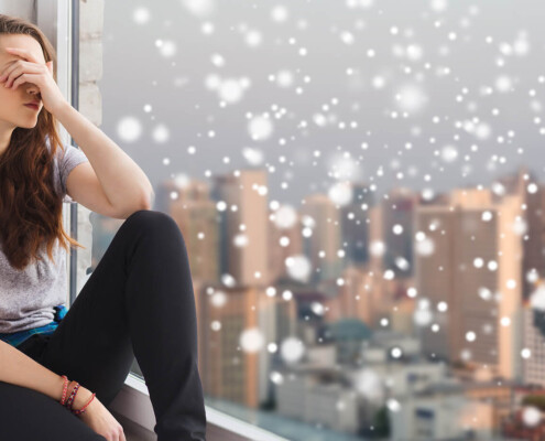 Teen sitting by a window with snow falling outside, looking overwhelmed during the holidays—an example of why cognitive behavioral therapy in chicago, il, cbt for anxiety in evanston, il, and a cbt therapist in evanston, il can help.
