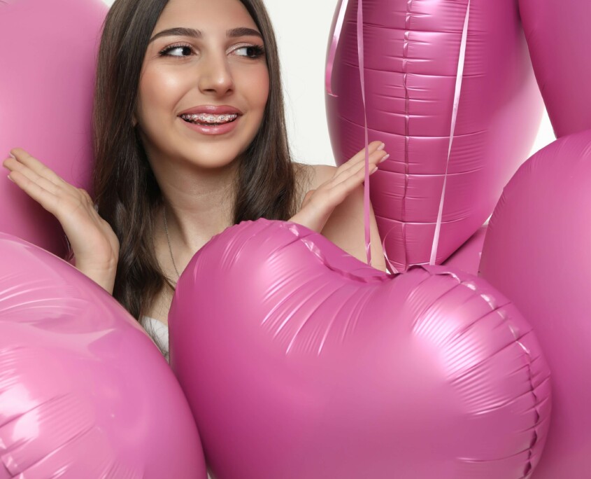 A smiling teen girl surrounded by pink heart-shaped balloons on Valentine's Day, representing the social pressure teens face that can be supported through therapy for teens in Chicago, IL and cognitive behavioral therapy in Chicago, IL.
