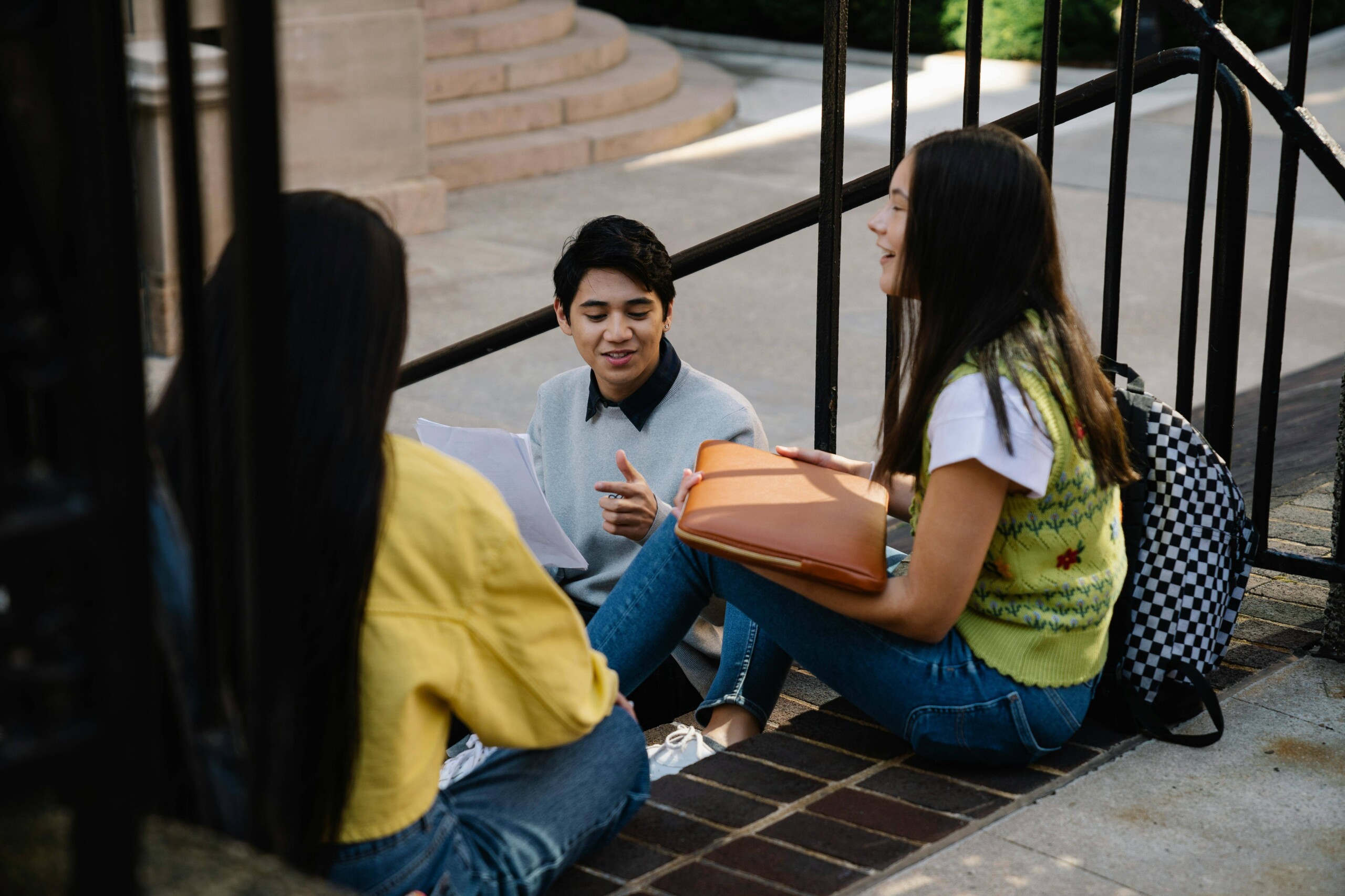 Three college students sitting together on campus steps having a conversation, representing the social connections that can ease overthinking with support from a therapist for college students in Chicago, IL and online therapy for moms in Chicago, IL.