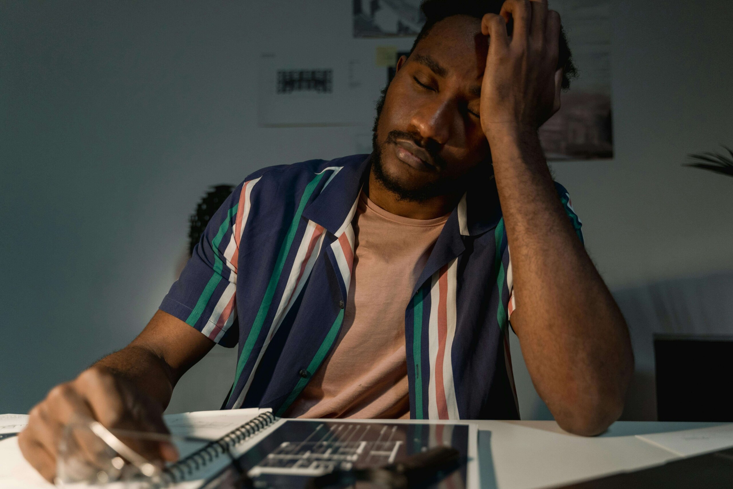A stressed college student holding his head while studying at a desk, illustrating the mental exhaustion of college burnout in Evanston, IL that can be addressed through cognitive behavioral therapy in Chicago, IL.