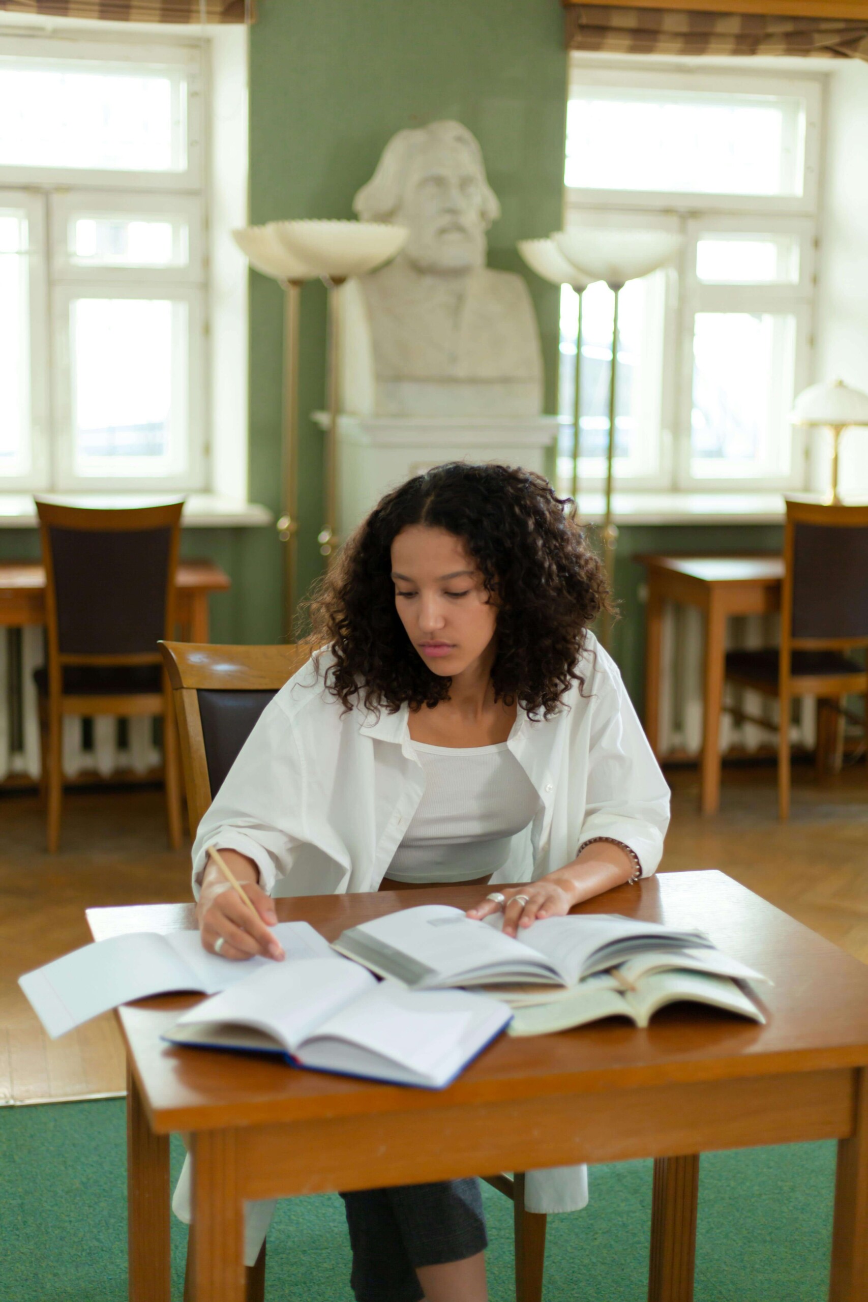 A college student studying alone in a library surrounded by multiple open textbooks, illustrating the overwhelming nature of academic pressure that can be addressed through therapy for young adults in Chicago, IL and online college counseling in Chicago, IL.