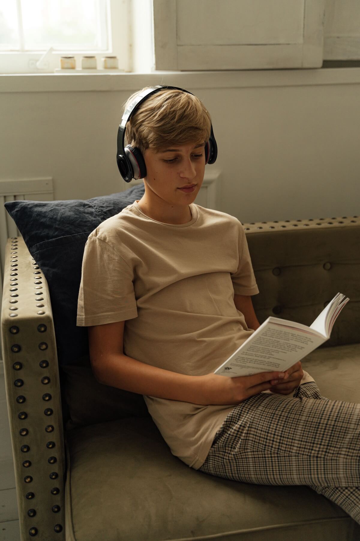 A teen wearing headphones and reading a book at home, representing the quiet moments of reflection and self-care supported through online therapy for teens in Chicago and online therapy for college students in Chicago, IL.