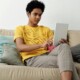 A teen sitting on a couch using a tablet at home, illustrating the accessibility of working with an online therapist for teens in Evanston, IL through online therapy for teenagers in Evanston, IL.