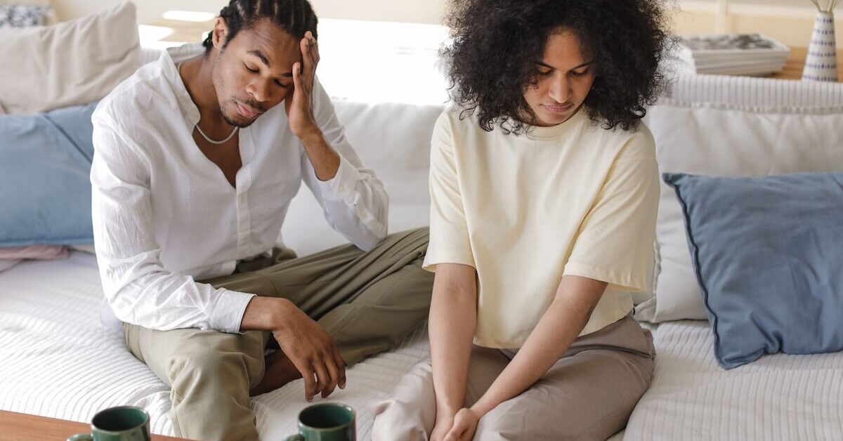 A couple sitting on a couch looking distressed and disconnected, representing the emotional strain that can be addressed through couples therapy in Evanston, IL with support from a couples therapist in Evanston, IL.