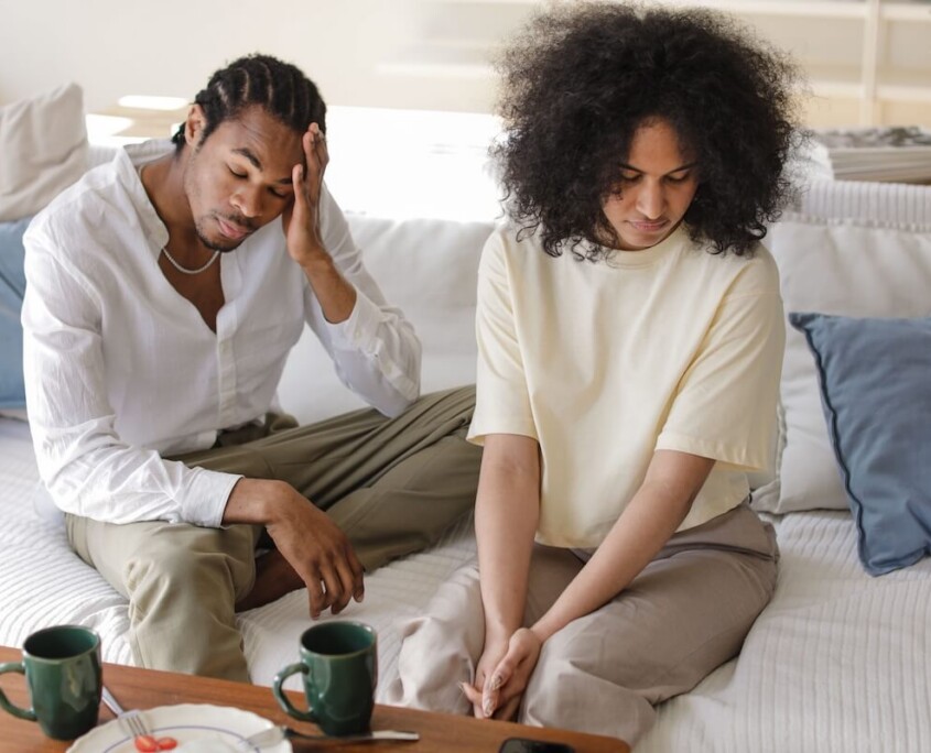 A couple sitting on a couch looking distressed and disconnected, representing the emotional strain that can be addressed through couples therapy in Evanston, IL with support from a couples therapist in Evanston, IL.