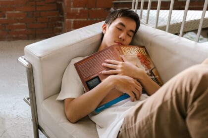 Exhausted from Anxiety | teen intervention evanston | evanston teen therapist | teenage intervention evanston, il | online therapy in illinois | Lincoln Park, IL | Downtown Evanston, IL | Central Street District, IL A teen boy asleep on a couch clutching a chemistry textbook, illustrating the exhaustion and overwhelm of school-related anxiety that can be addressed through anxiety therapy in Evanston and teen intervention in Evanston.