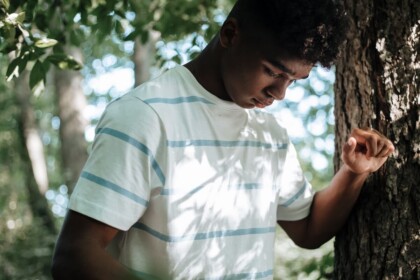 Upset Teen Boy | teenage intervention evanston, il | evanston teen therapist | anxiety in evanston, il | online therapy in illinois | Rogers Park, IL | Streeterville, IL | Northwestern University, IL A teen boy leaning against a tree with a thoughtful, downcast expression, representing the internal struggle behind school avoidance that can be supported through an Evanston teen therapist or teenage intervention in Evanston, IL.